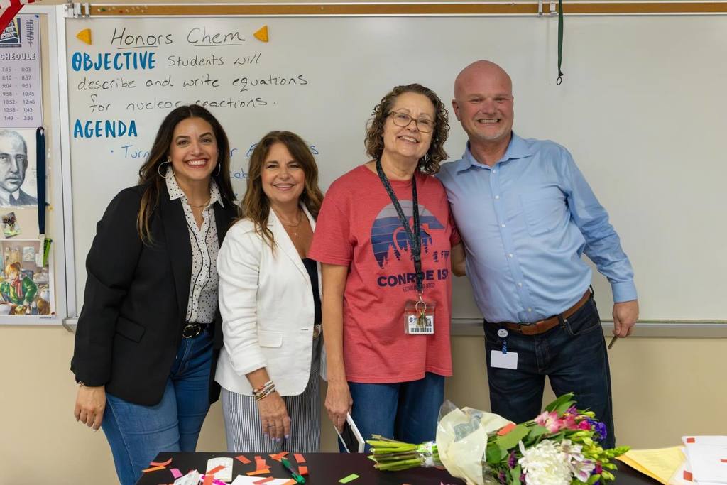 Superintendent and two board members congratulate staff member.