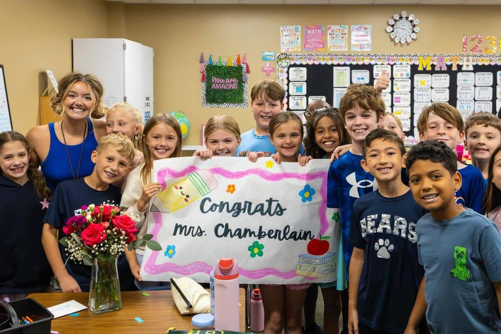 Students hold up sign congratulating teacher on award.