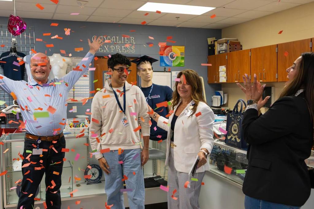 Superintendent and two board members congratulate student as confetti falls.