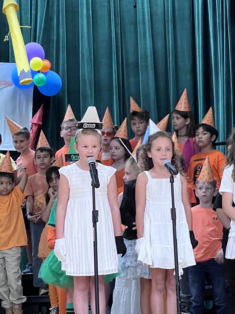 two girls dressed in white standing at microphones during program