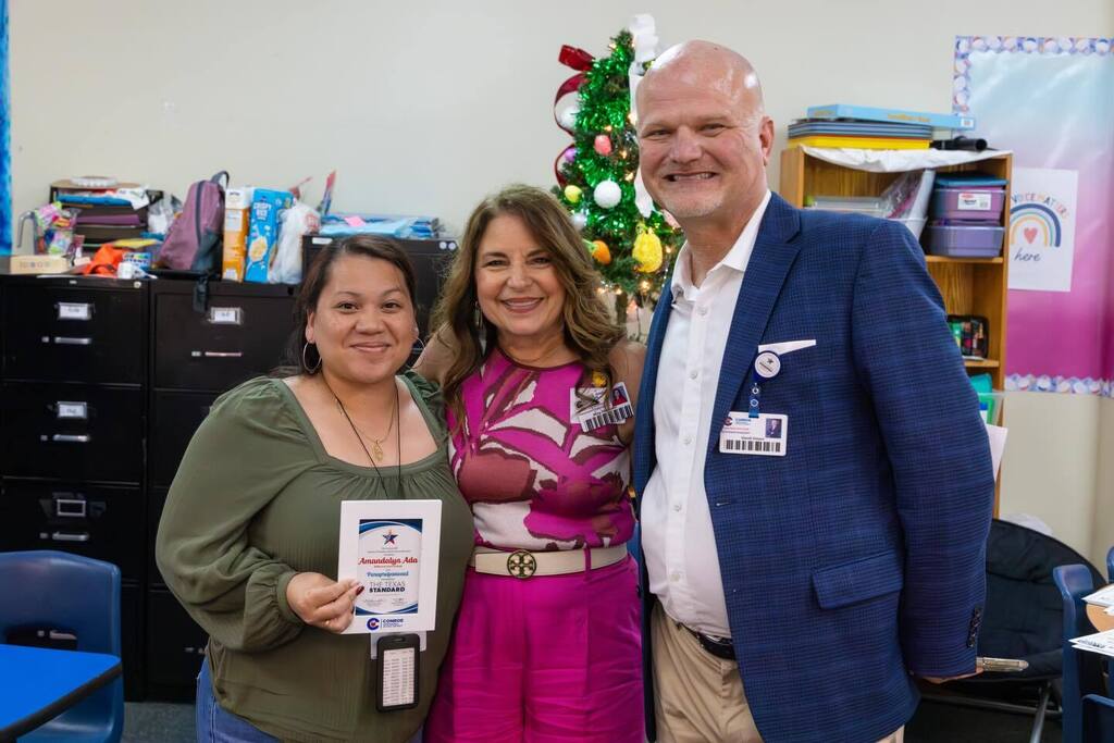 Staff member holds award plaque and is joined by Board President and Superintendent.