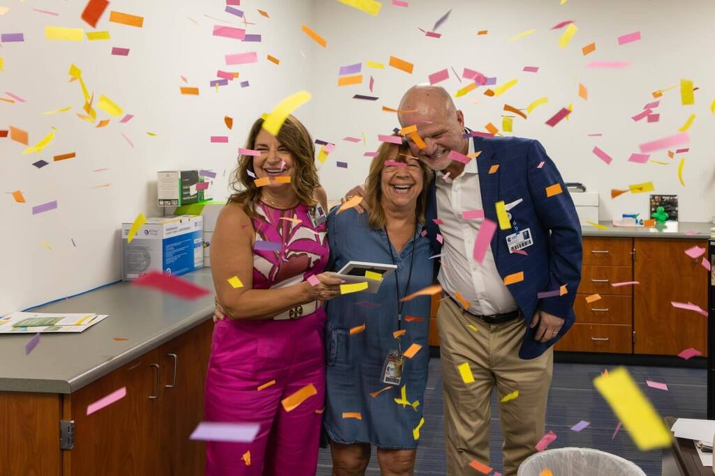 Staff member laughs with Board President and Superintendent as confetti falls.