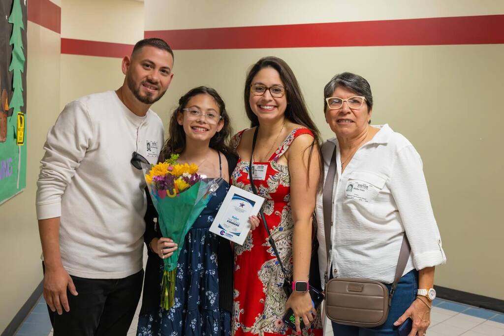 Student holding award plaque and flowers joined by family.