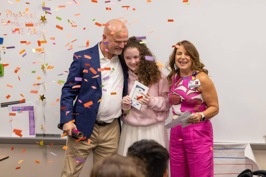 Student holds award plaque and is joined by Superintendent and Board President as confetti falls.
