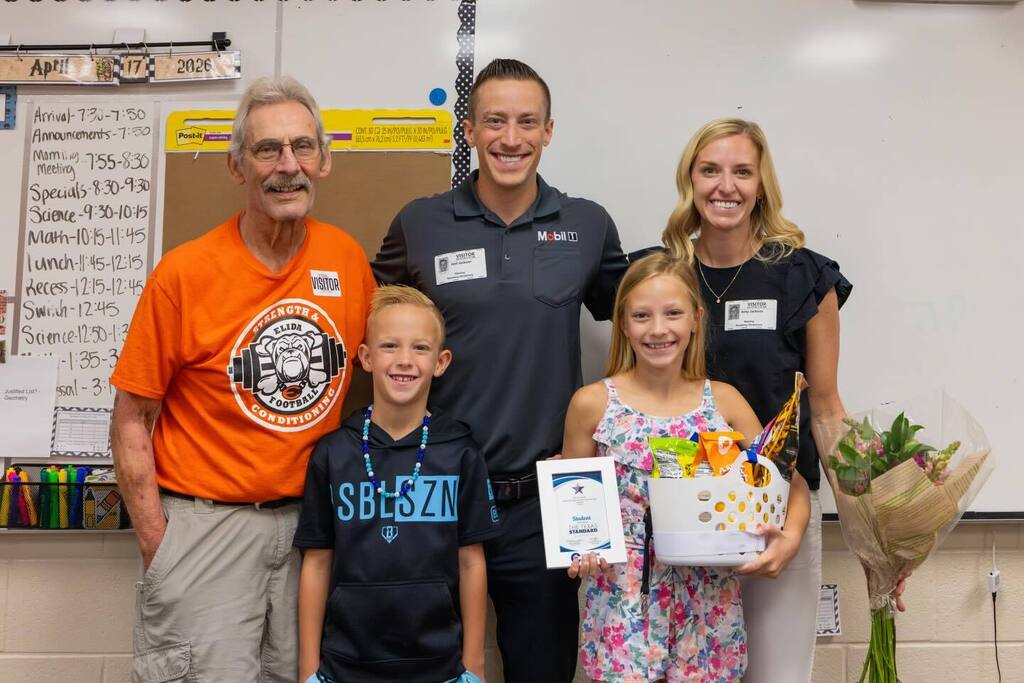 Student holding award plaque and gift basket joined by family.