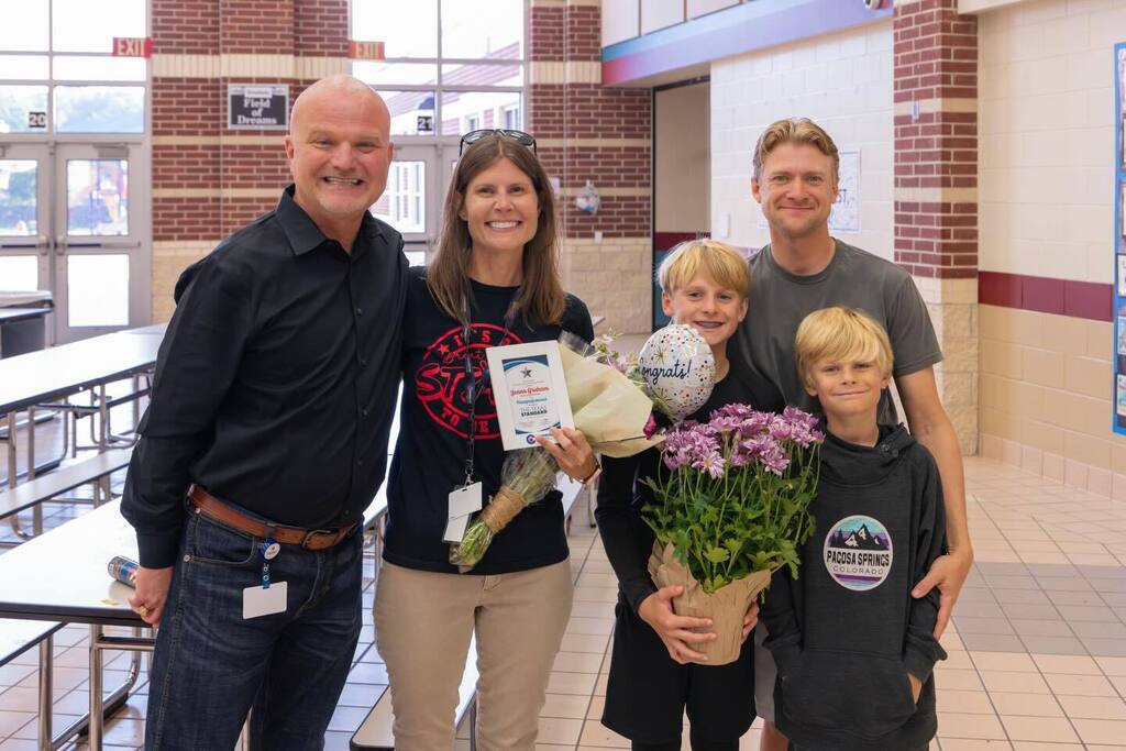 Staff member holding award plaque joined by family and Superintendent.