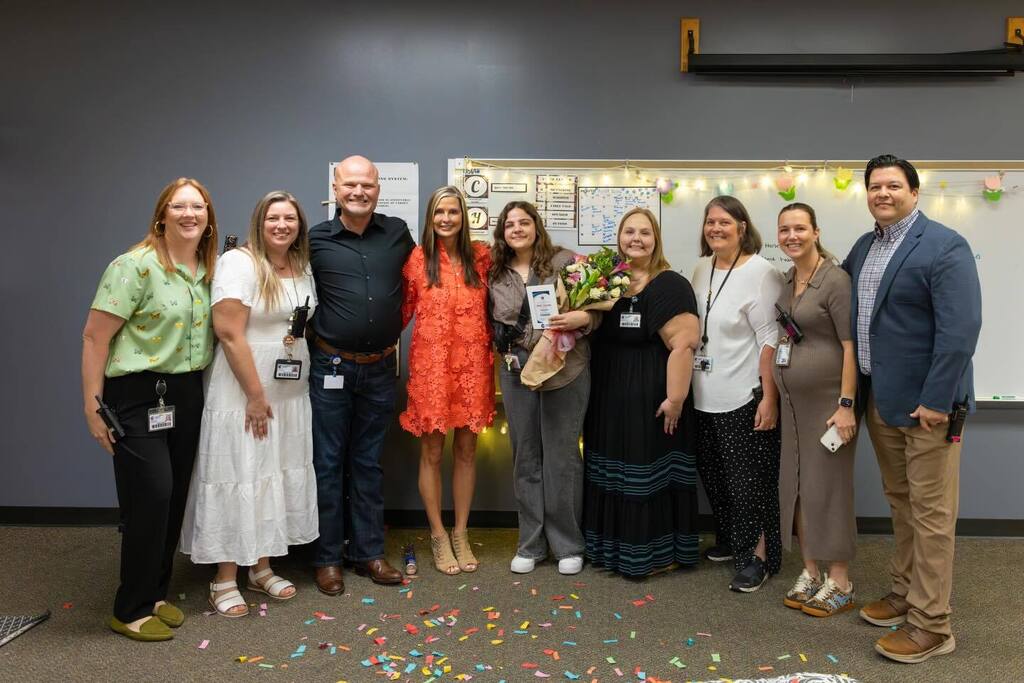 Staff member holds award plaque and flowers joined by colleagues.