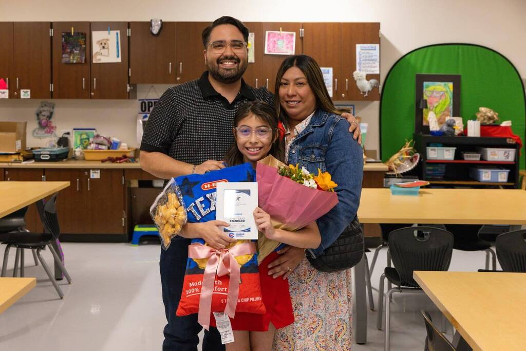 Student holds award plaque, flowers and gifts joined by family.