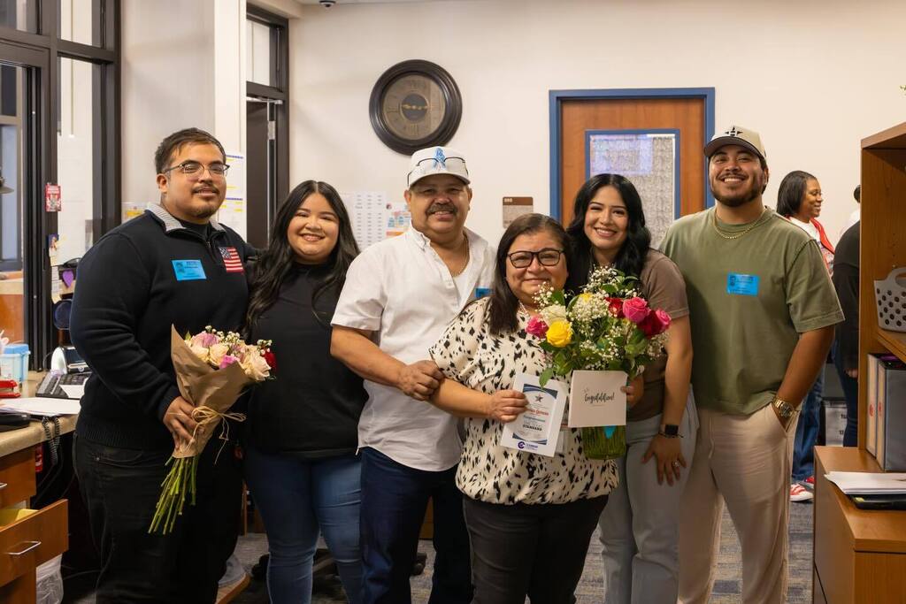 Staff member holds award plaque and flowers joined by family.
