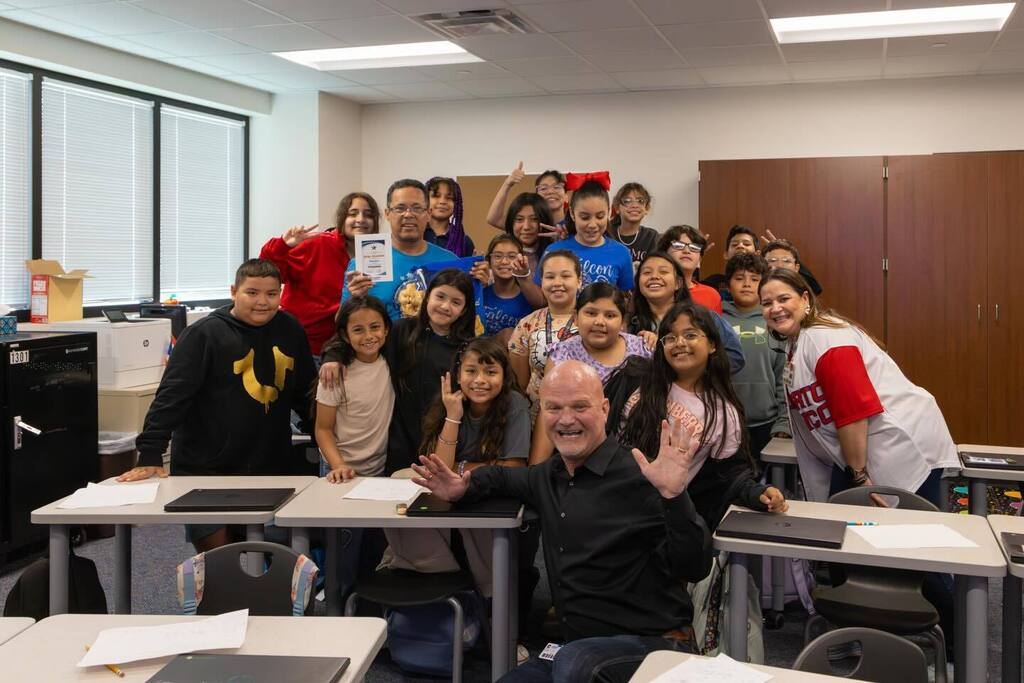 Teacher holds award plaque and is surrounded by students with Superintendent in front.