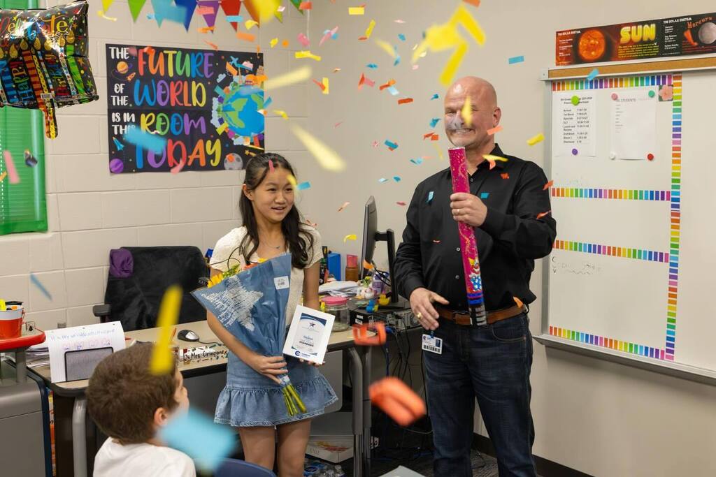 Student holds award plaque as Superintendent pops confetti.