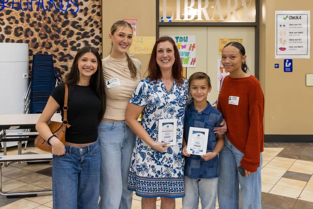 Staff member and student hold award plaques and joined by family.