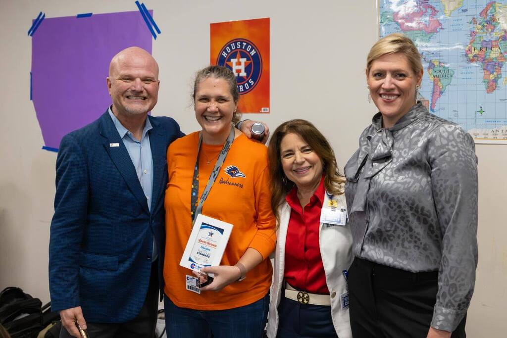 Educator holding award plaque joined by Superintendent and two board members.