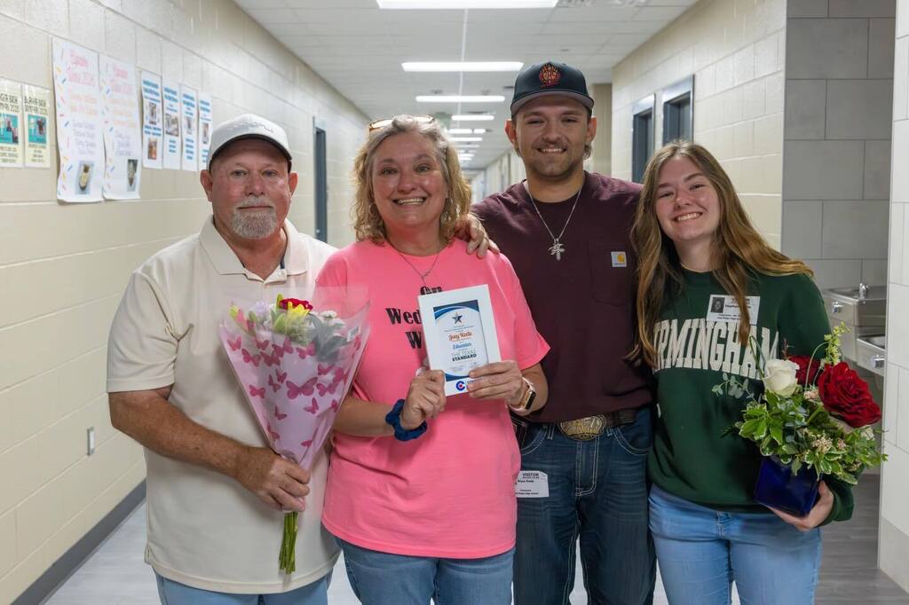 Educator holding award plaque joined by family holding flowers.