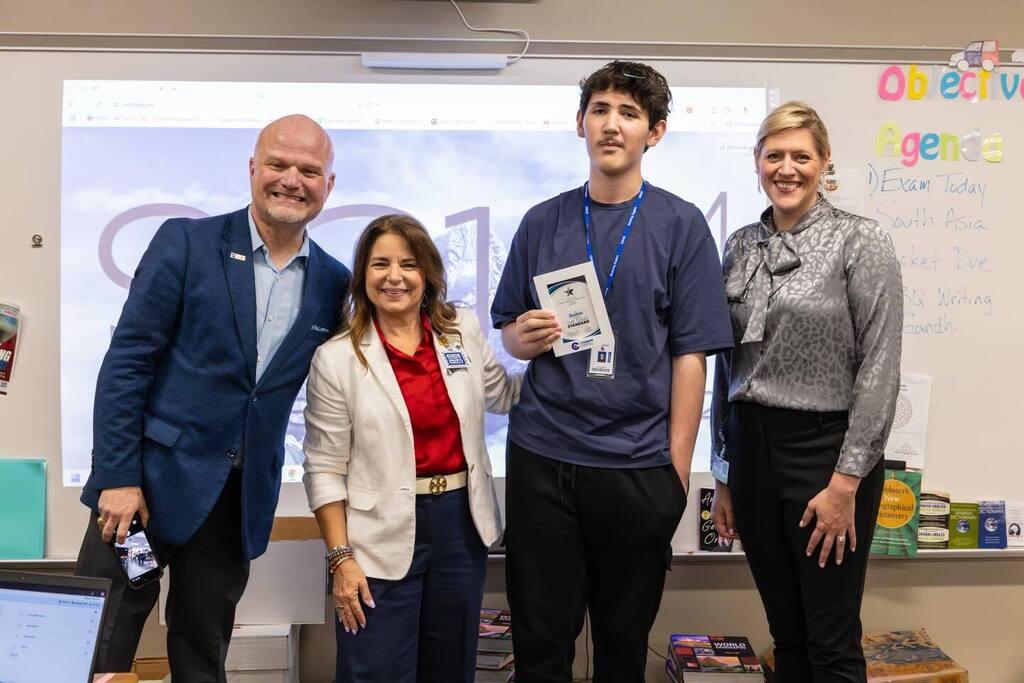Student holding award plaque joined by Superintendent and two board members.