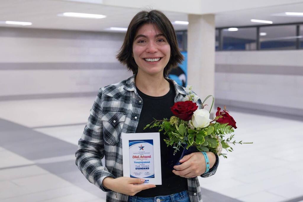 Staff member smiling holding award plaque and flowers.
