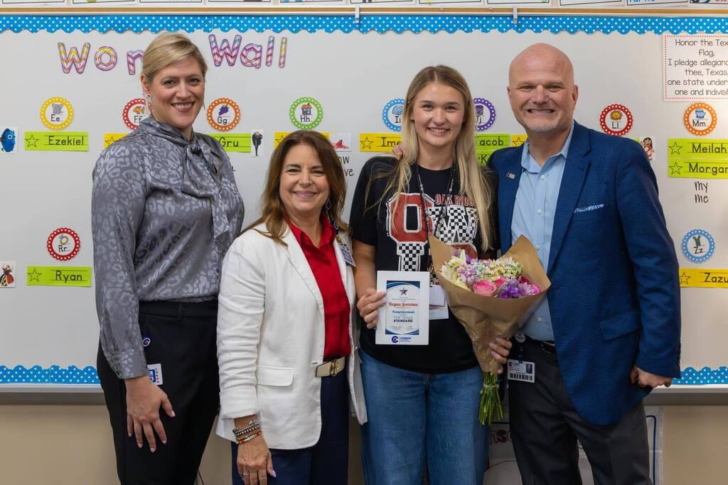 Staff member holding award plaque and flowers joined by Superintendent and two board members.
