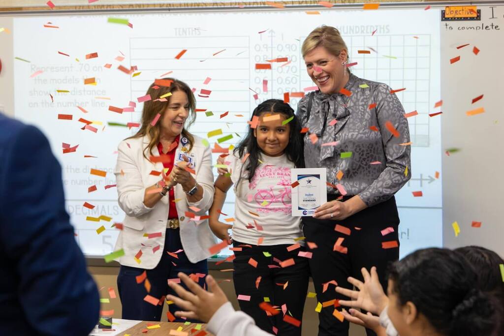 Student given award plaque by two board members as confetti falls.