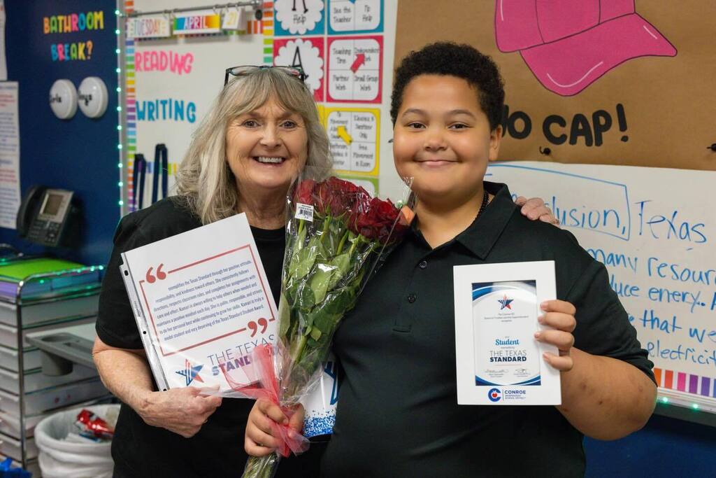 Student holding award plaque and flowers joined by teacher.