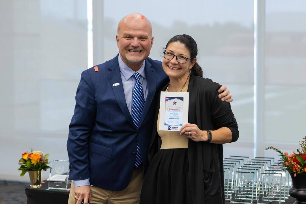 Staff member holding award plaque hugs Superintendent.