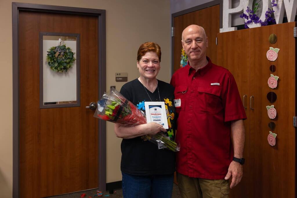 Staff member holding award plaque and flowers joined by family member.