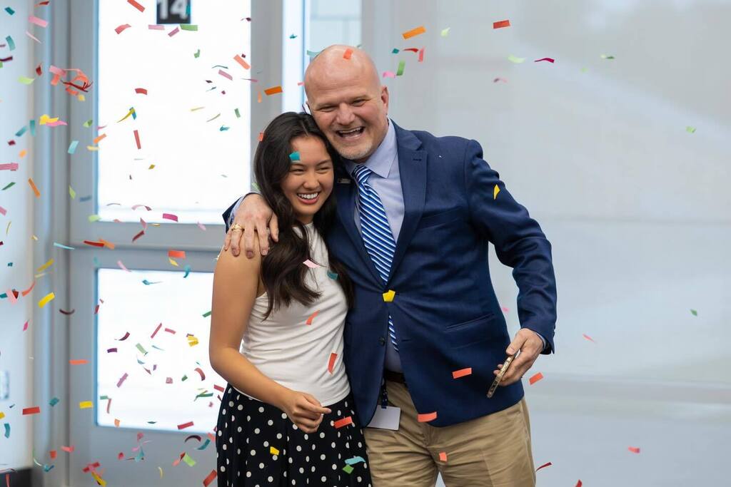 Student laughs with Superintendent as confetti falls.