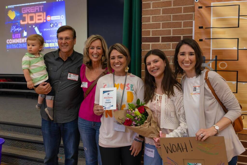 Teacher holding award plaque and flowers joined by family.