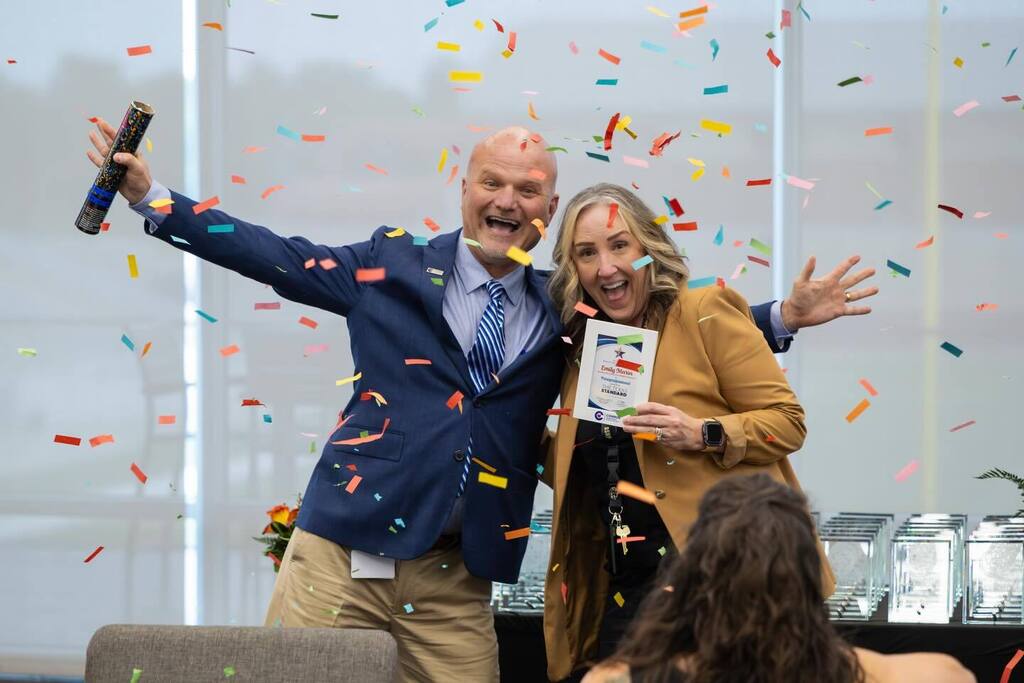 Staff member holding award plaque laughs with Superintendent as confetti falls.
