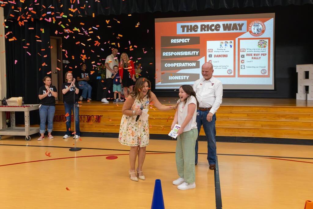 Student holding award surprised by confetti and congratulated by Board President and Superintendent.