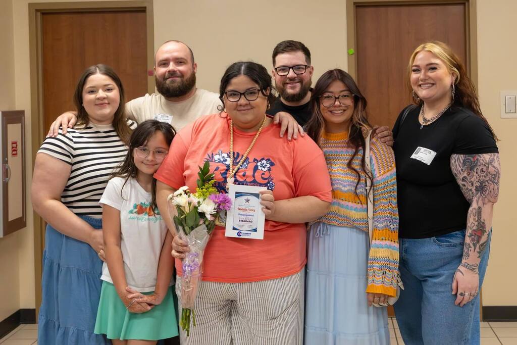 Staff member holding award plaque and flowers joined by family.
