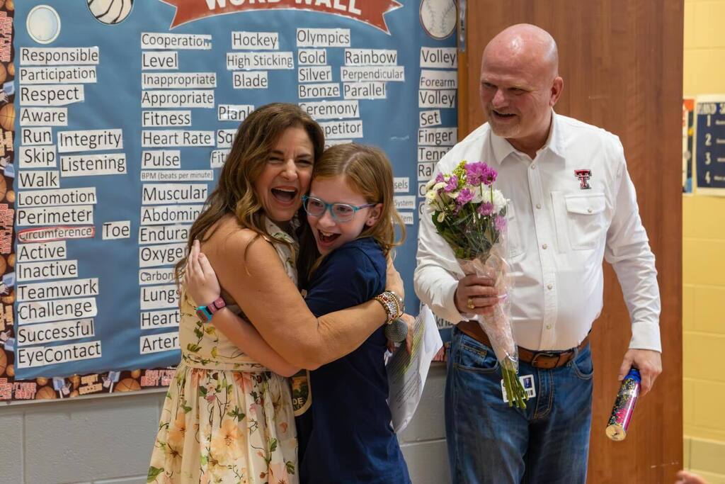 Student hugs Board President as she is presented with award and flowers by Superintendent.