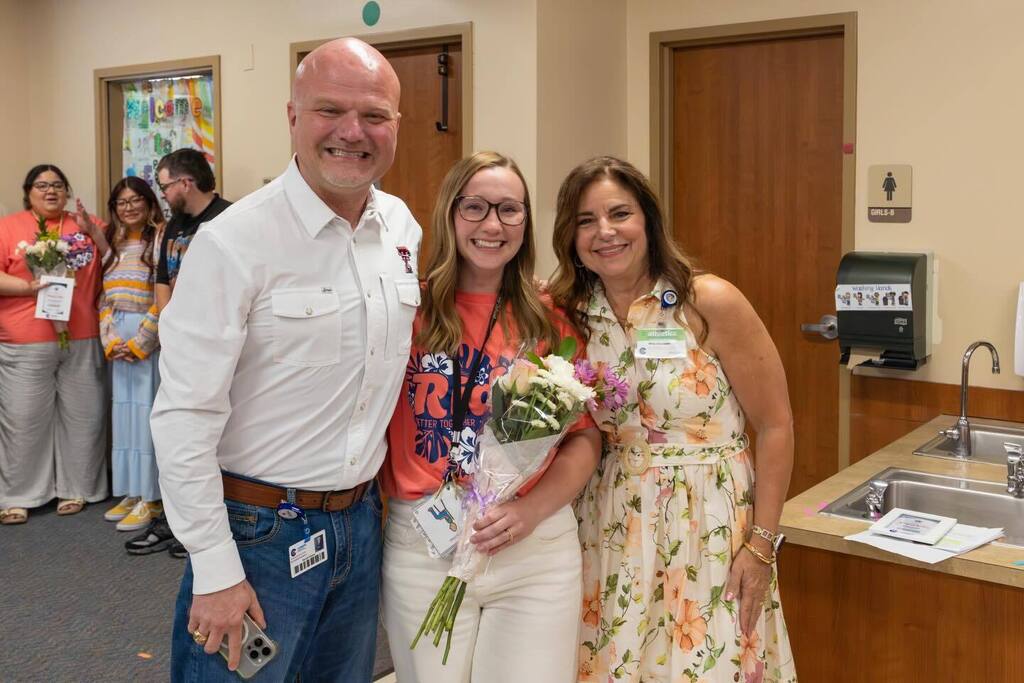 Staff member holds flowers as she is congratulated by Superintendent and Board President.