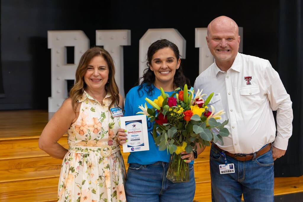Staff member holding award and flowers joined by Board President and Superintendent.