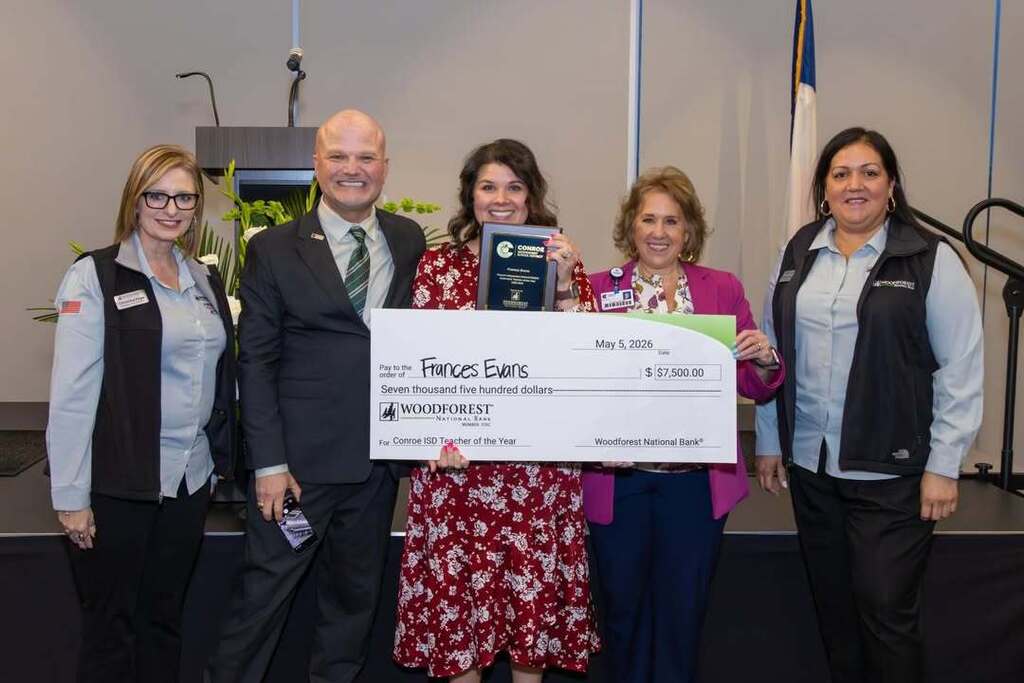 Teacher holding a giant check and award joined by administrators and sponsors.