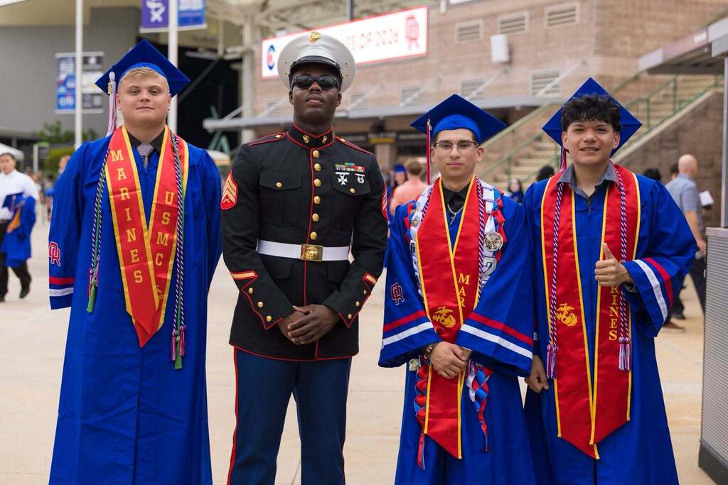 Three graduates in blue robes and Marines sashes with Marine.