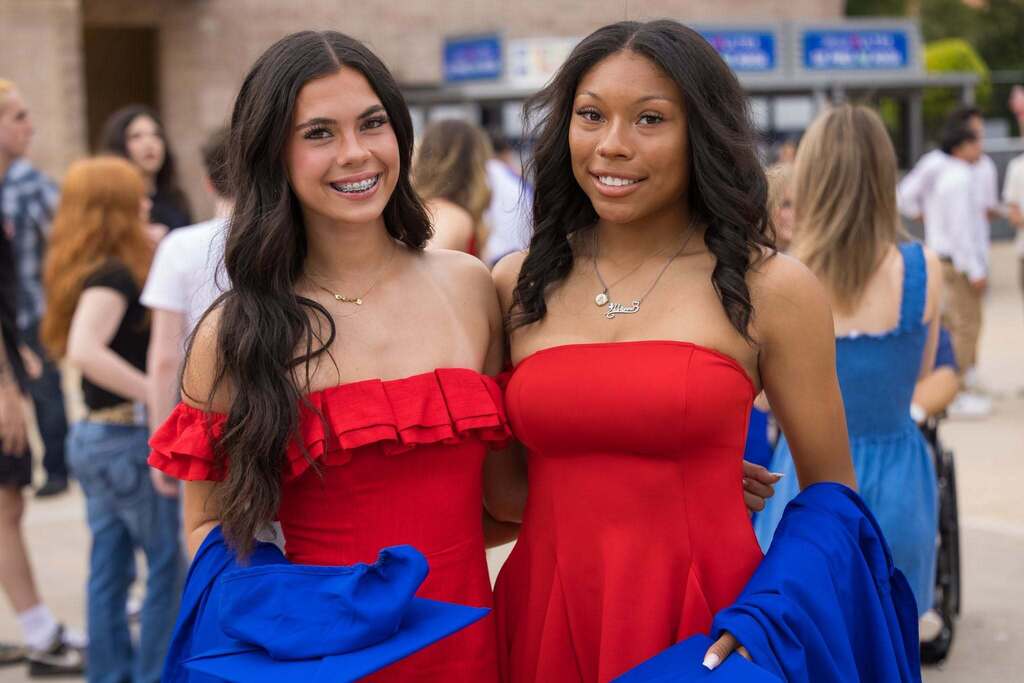 Two female students in red dresses holding blue graduation robes.