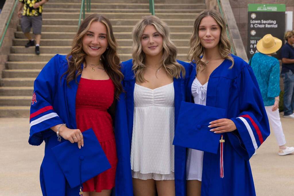 Three female graduates in dresses and blue robes.