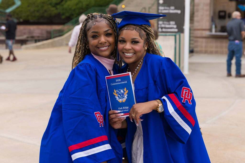 Two female graduates in blue robes with commencement program.