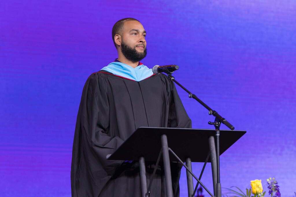 Principal gives speech at graduation in front of purple background.