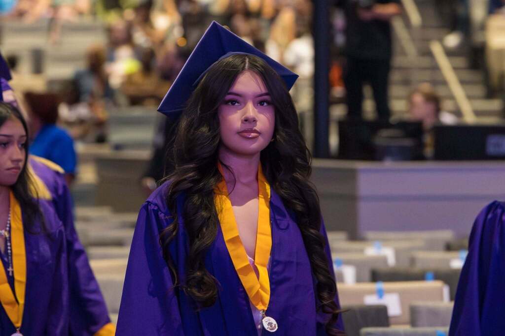 Senior in purple robe walks to her seat at graduation ceremony.