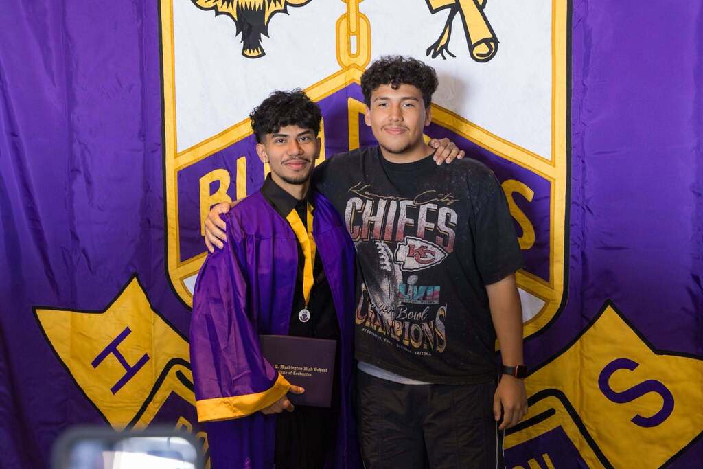 Graduate hugs family member in front of school crest.