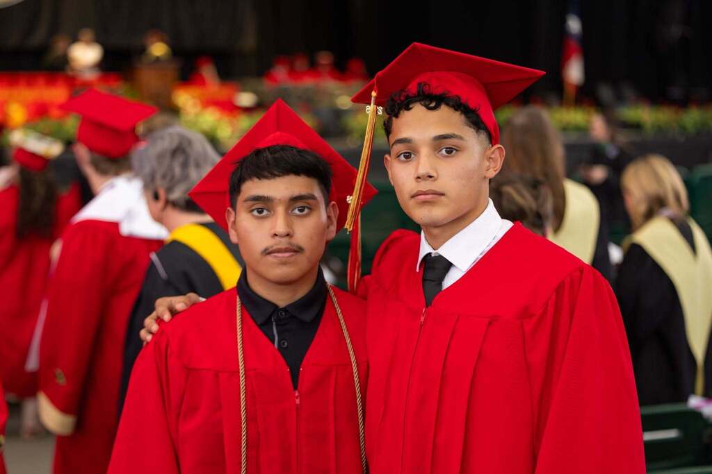 Two male graduates in red caps and gowns.