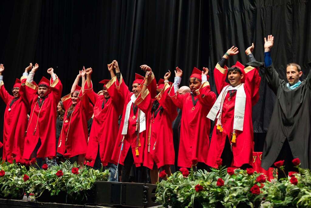 Graduates in red robes hold up hands.