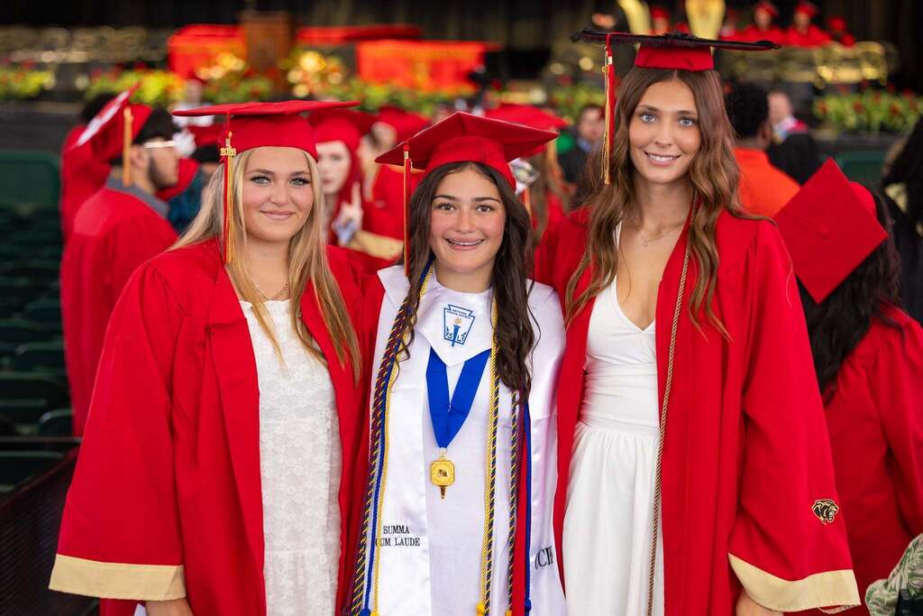 Three female graduates in white dresses and red caps and gowns.