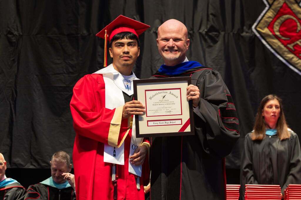 Valedictorian and Superintendent hold award plaque.