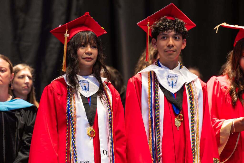 Male and female graduate stand during graduation ceremony.