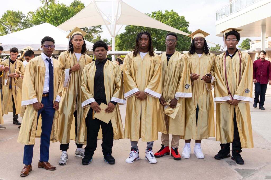 Seven male graduates in gold caps and gowns.