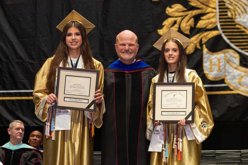 Valedictorian and salutatorian hold awards with Superintendent.