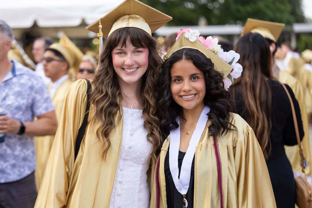 Two female students in gold caps and gowns.
