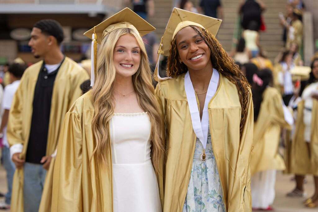 Two female graduates in white dresses and gold caps and gowns.